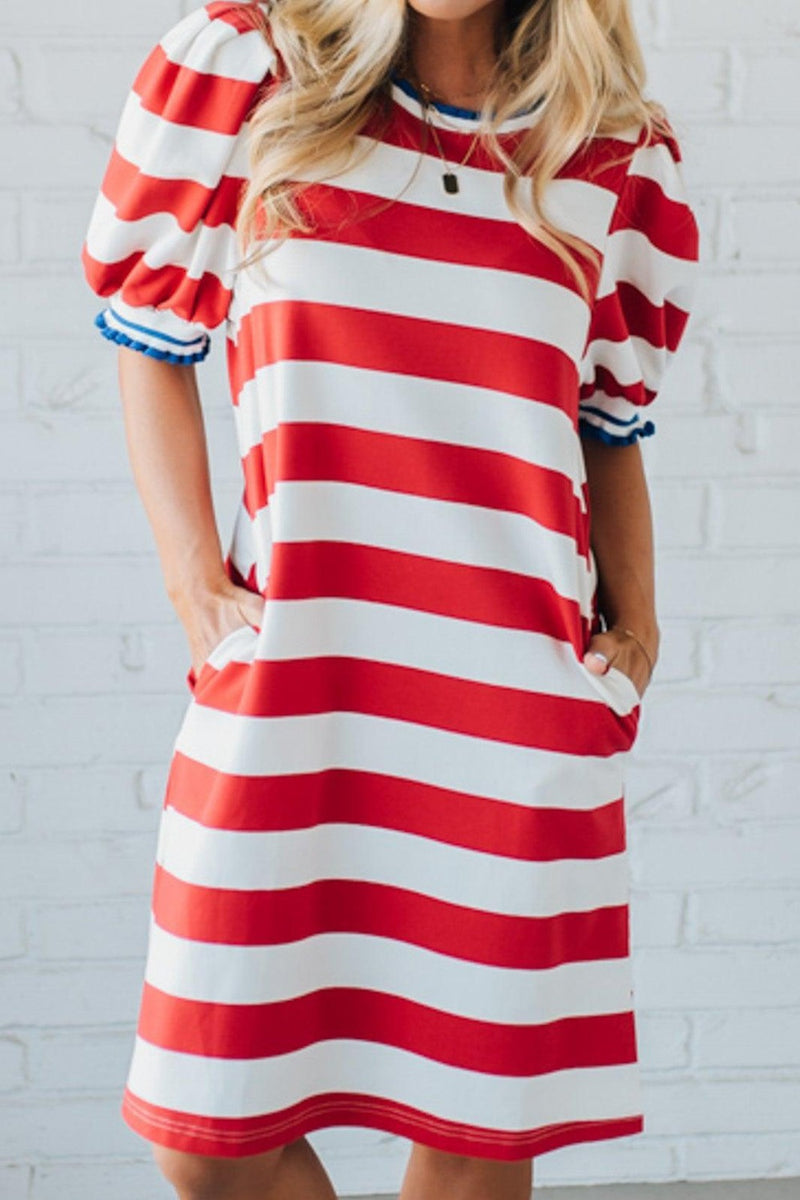 Red and white striped dress worn by a person against a white brick wall.