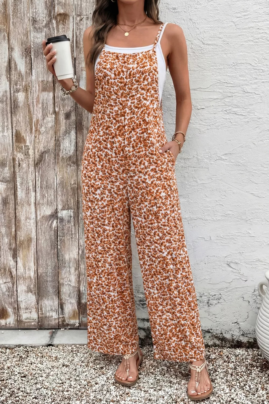 Woman wearing a leopard print jumpsuit holding a coffee cup against a wooden and white brick wall.