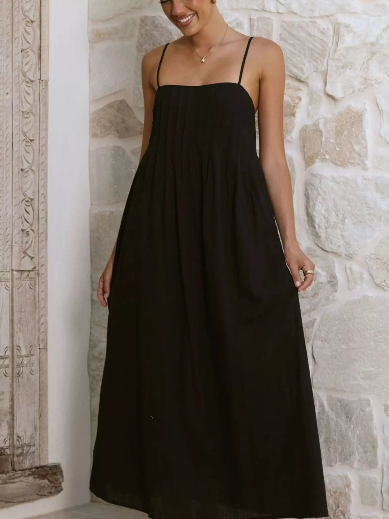 Woman wearing a black slip dress against a stone wall.