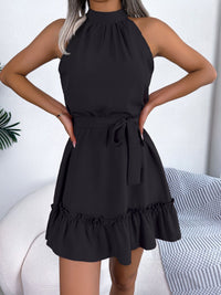 Black halter neck dress with ruffled hem worn by a person, sitting on a white couch.