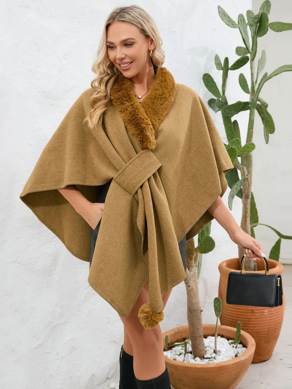 Woman wearing a brown poncho with fur collar standing next to potted plants.