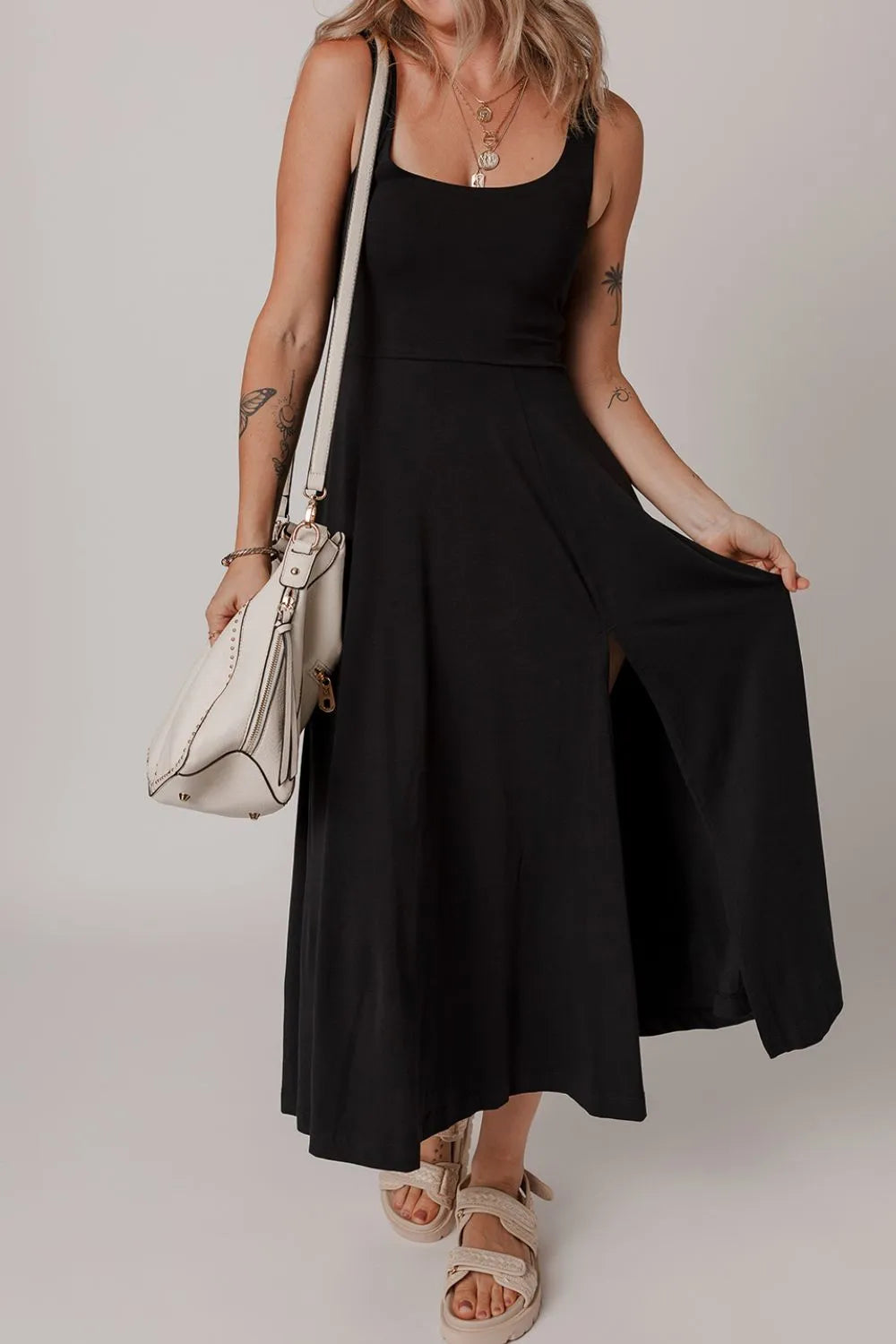 Woman wearing a black sleeveless dress holding a white handbag on a plain background