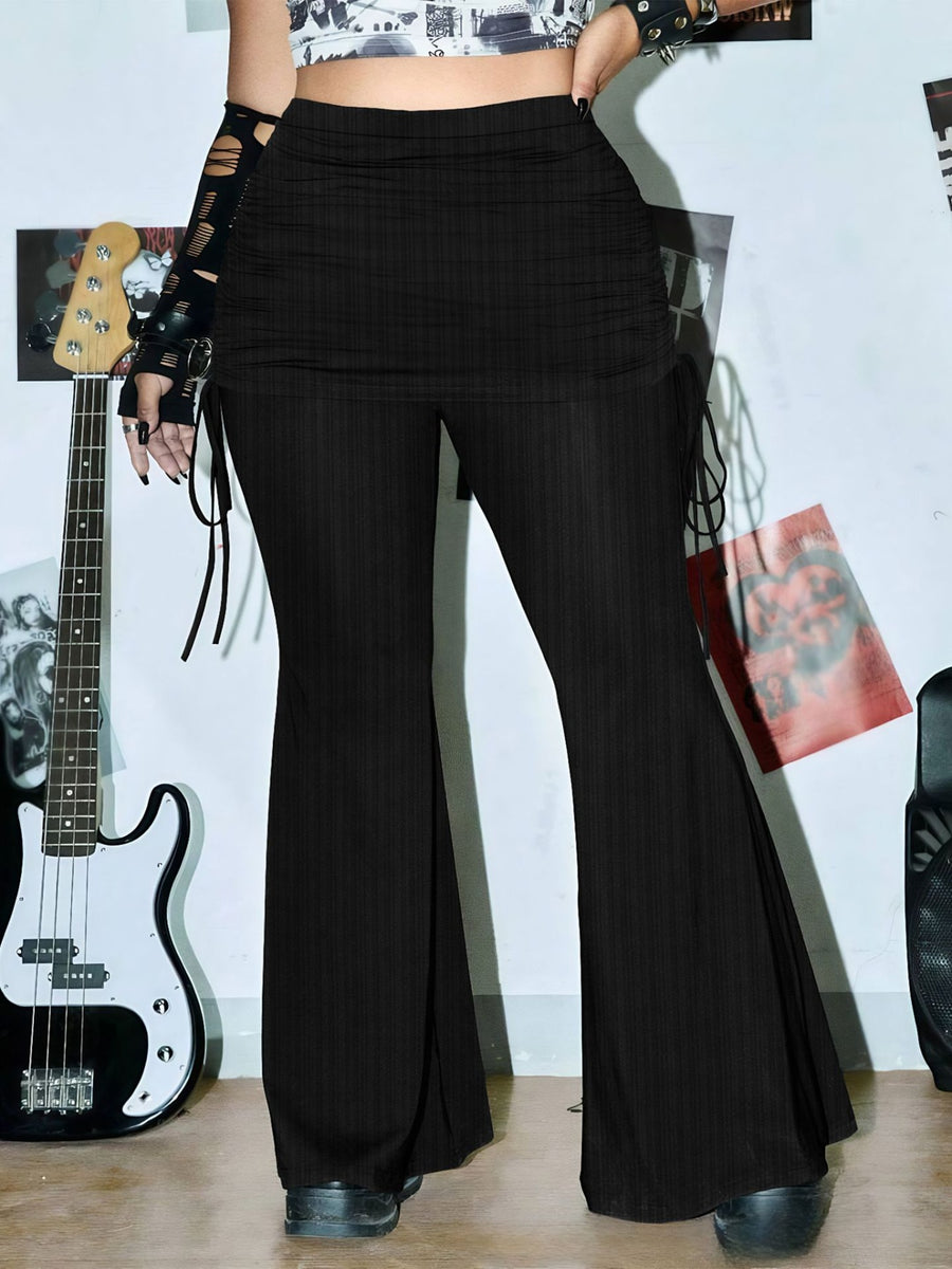 Person wearing black flared pants with a guitar and other musical instruments in the background