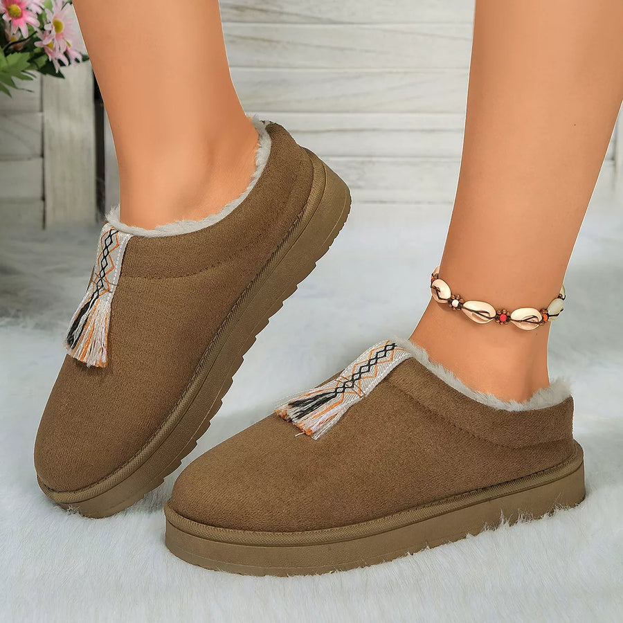 Brown slip-on shoes with fringes worn by a person on a white background