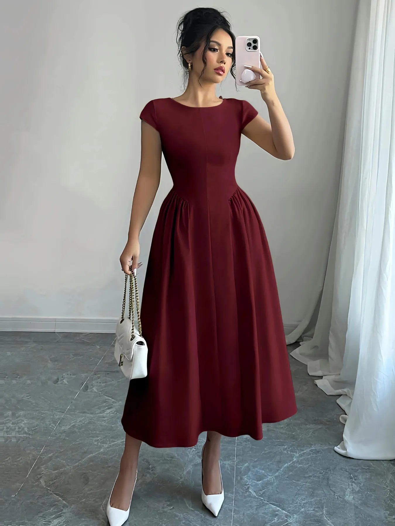 Woman taking a mirror selfie wearing a burgundy dress with a white handbag.