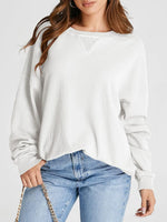 Woman wearing a white long-sleeve top and blue jeans on a plain background