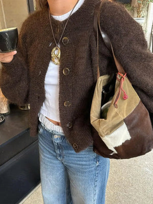 Person wearing a brown cardigan, white shirt, blue jeans, and holding a patterned bag.
