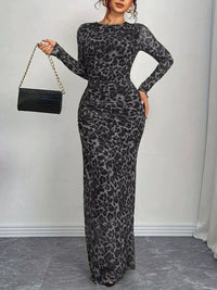 Woman wearing a gray leopard print dress holding a black handbag against a white wall.