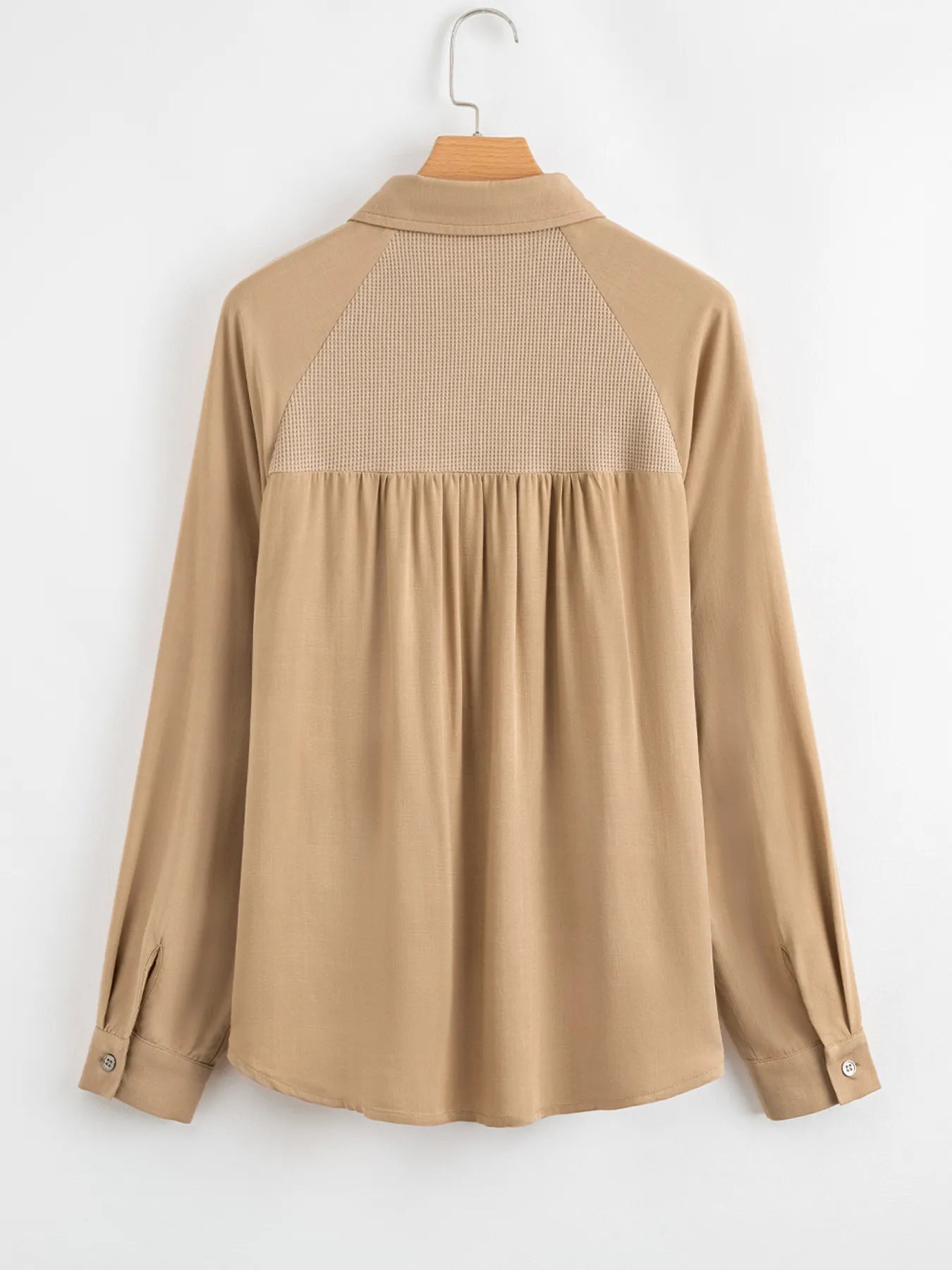 Beige blouse with a textured back panel on a hanger against a white background
