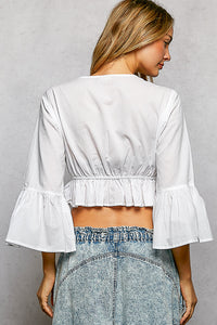 Woman wearing a white blouse with ruffled sleeves and denim shorts on a gray background