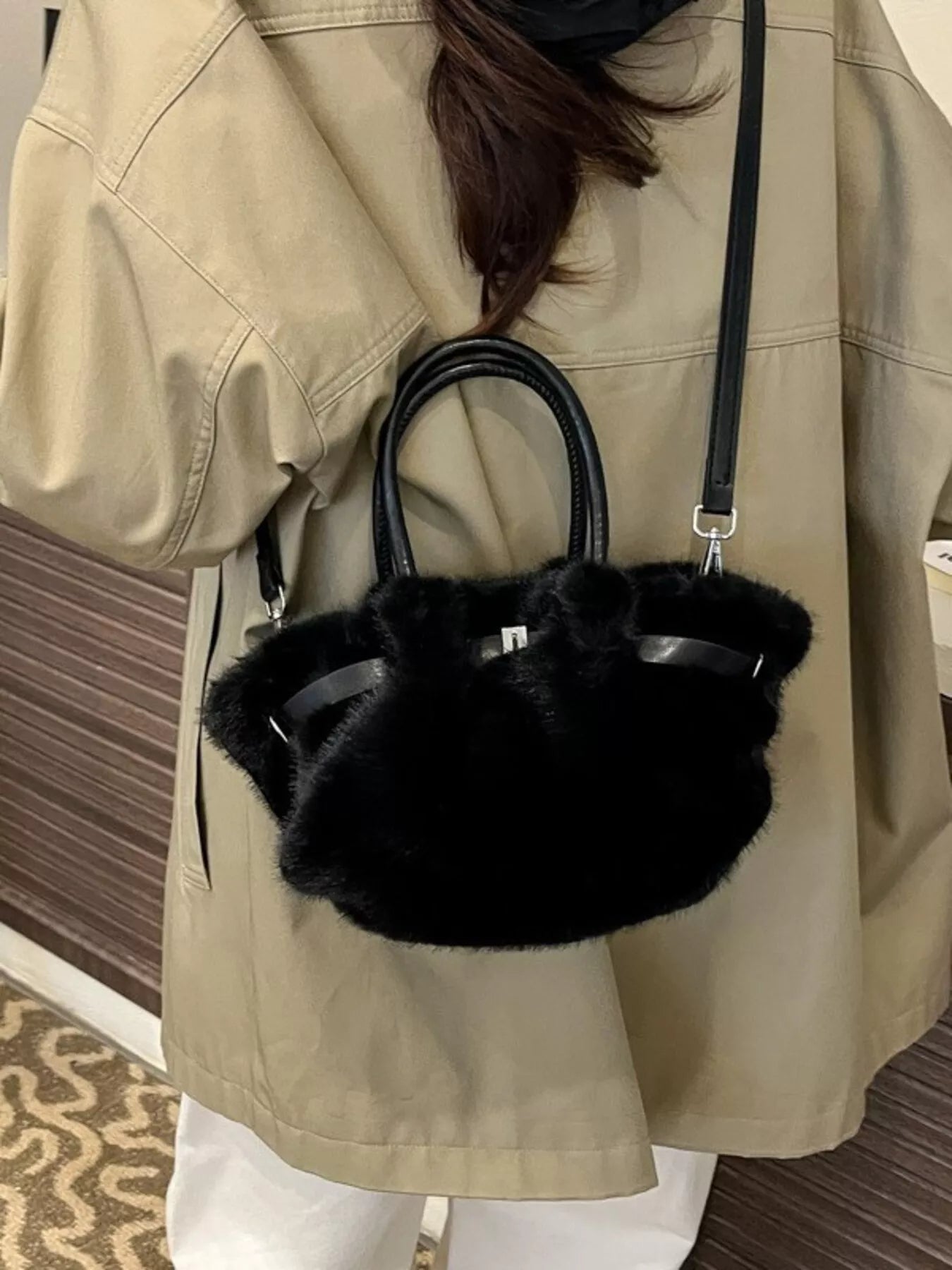 Person wearing a beige coat holding a black fur handbag.