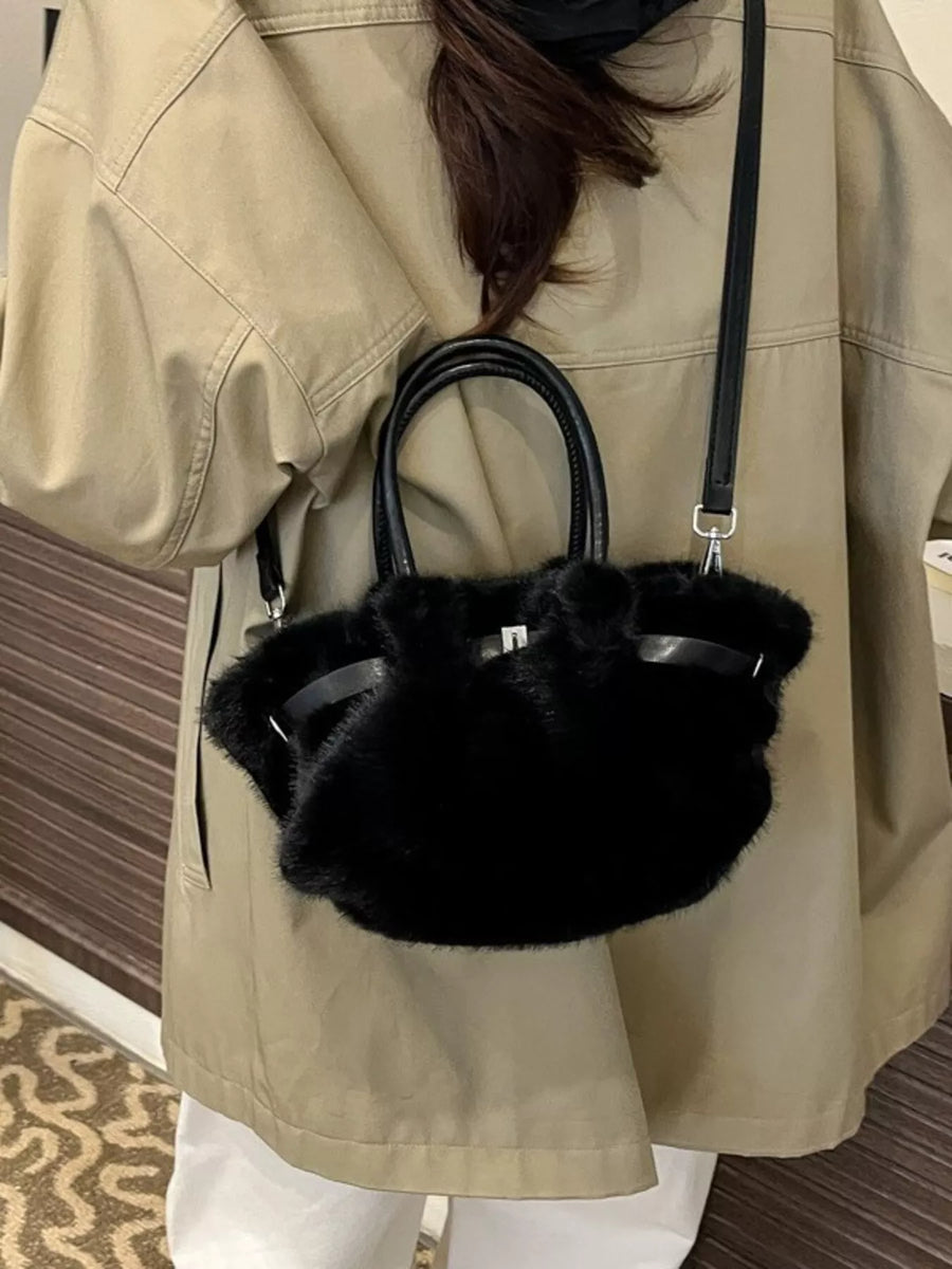 Person wearing a beige coat holding a black fur handbag.