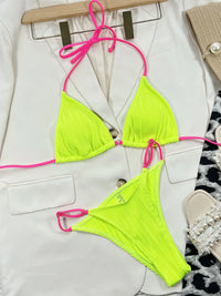 Neon green bikini set with pink straps on a white surface.