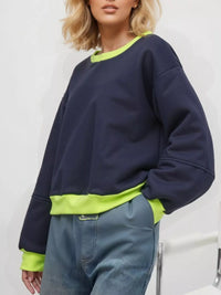 Person wearing a navy sweatshirt with green accents and blue jeans on a white background