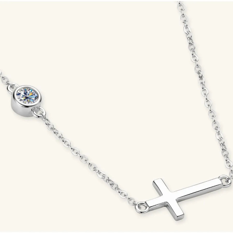 Silver necklace with a cross pendant and round gemstone on a white background