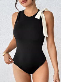 Black swimsuit with a white bow on a plain background