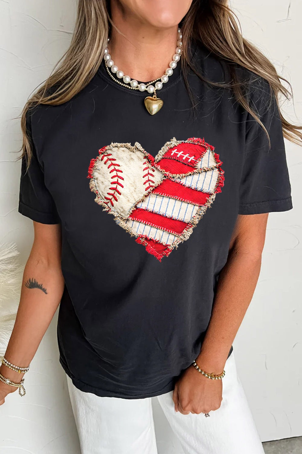 Black t-shirt with a heart design featuring a baseball and football, worn by a person.