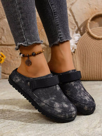 Black clogs worn with gray jeans on a stone surface.