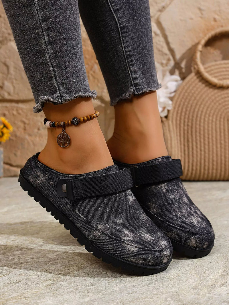 Black clogs worn with gray jeans on a stone surface.