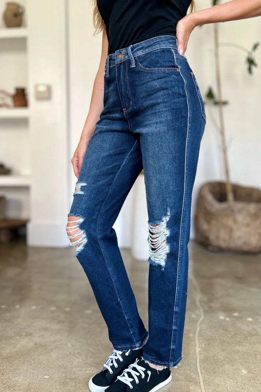 Person wearing blue jeans with slight distressing in a room setting.