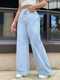Person wearing light blue jeans standing outdoors near a building.