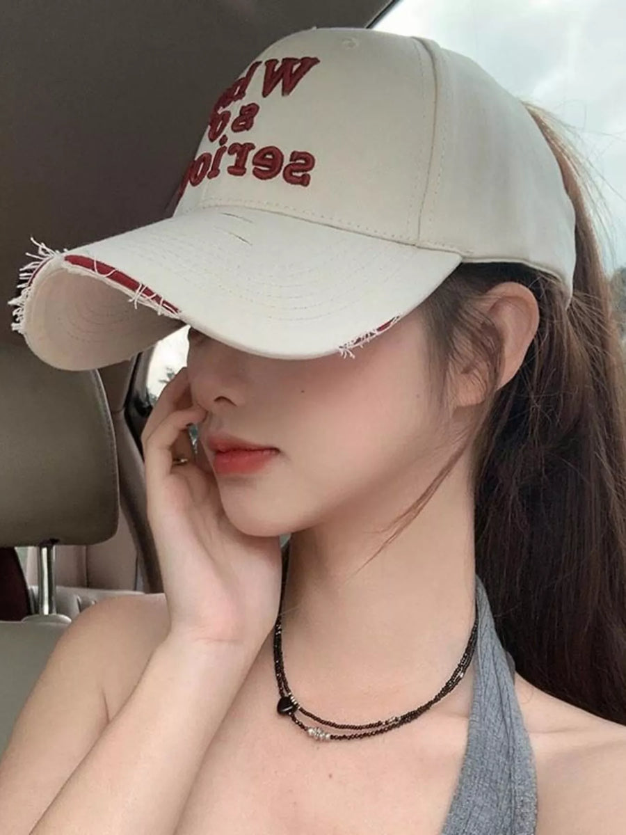 Woman wearing a beige cap with red text, sitting inside a vehicle.