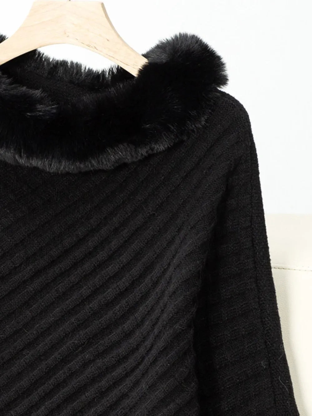 Black poncho with fur trim on a hanger against a white background