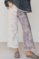 Person wearing floral and leopard print pants with a dark jacket against a white wall.