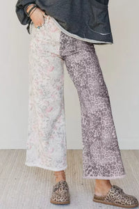 Person wearing floral and leopard print pants with a dark jacket against a white wall.