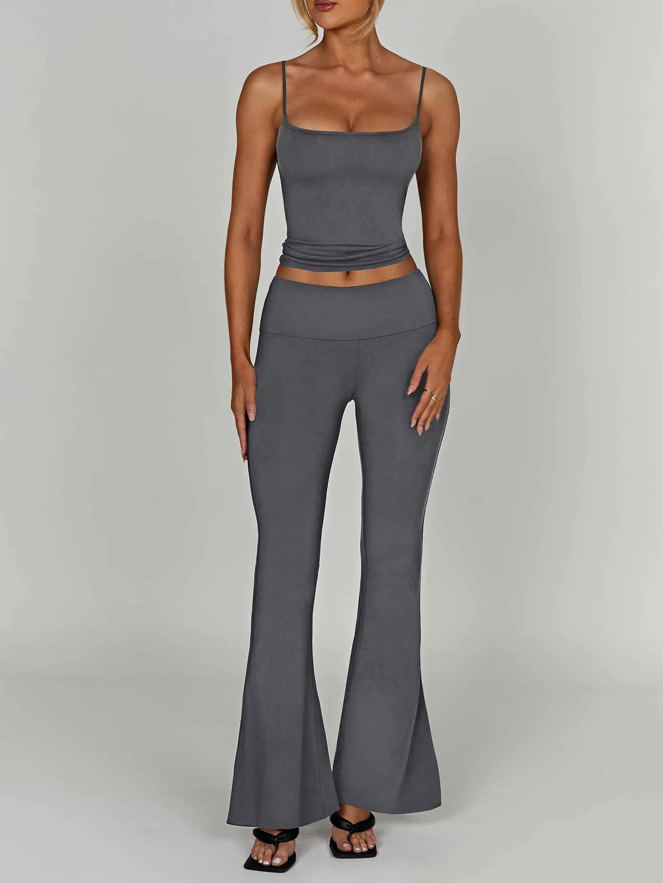 Woman wearing a gray sleeveless top and flared pants on a plain background