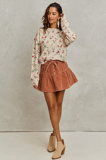 Woman wearing a floral sweater and brown skirt against a plain background