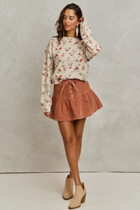 Woman wearing a floral sweater and brown skirt against a plain background