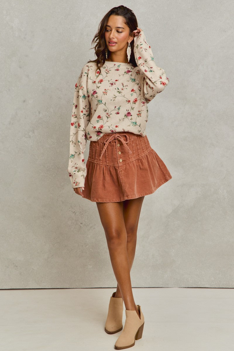 Woman wearing a floral sweater and brown skirt against a plain background
