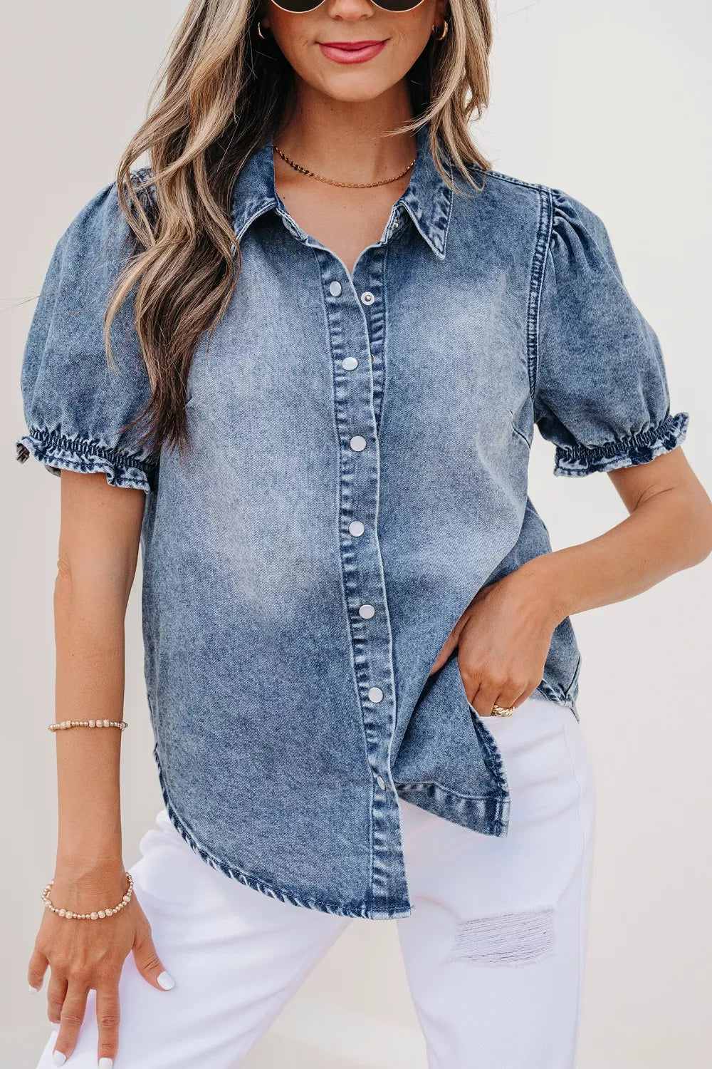 Woman wearing a denim shirt with white pants against a plain background