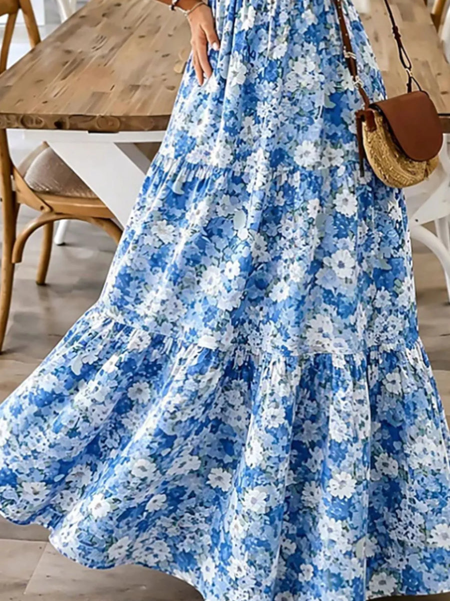Woman wearing a blue floral dress with a wooden table and chair in the background