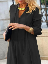 Woman wearing a black dress with a yellow necklace and gold watch, holding a black clutch.
