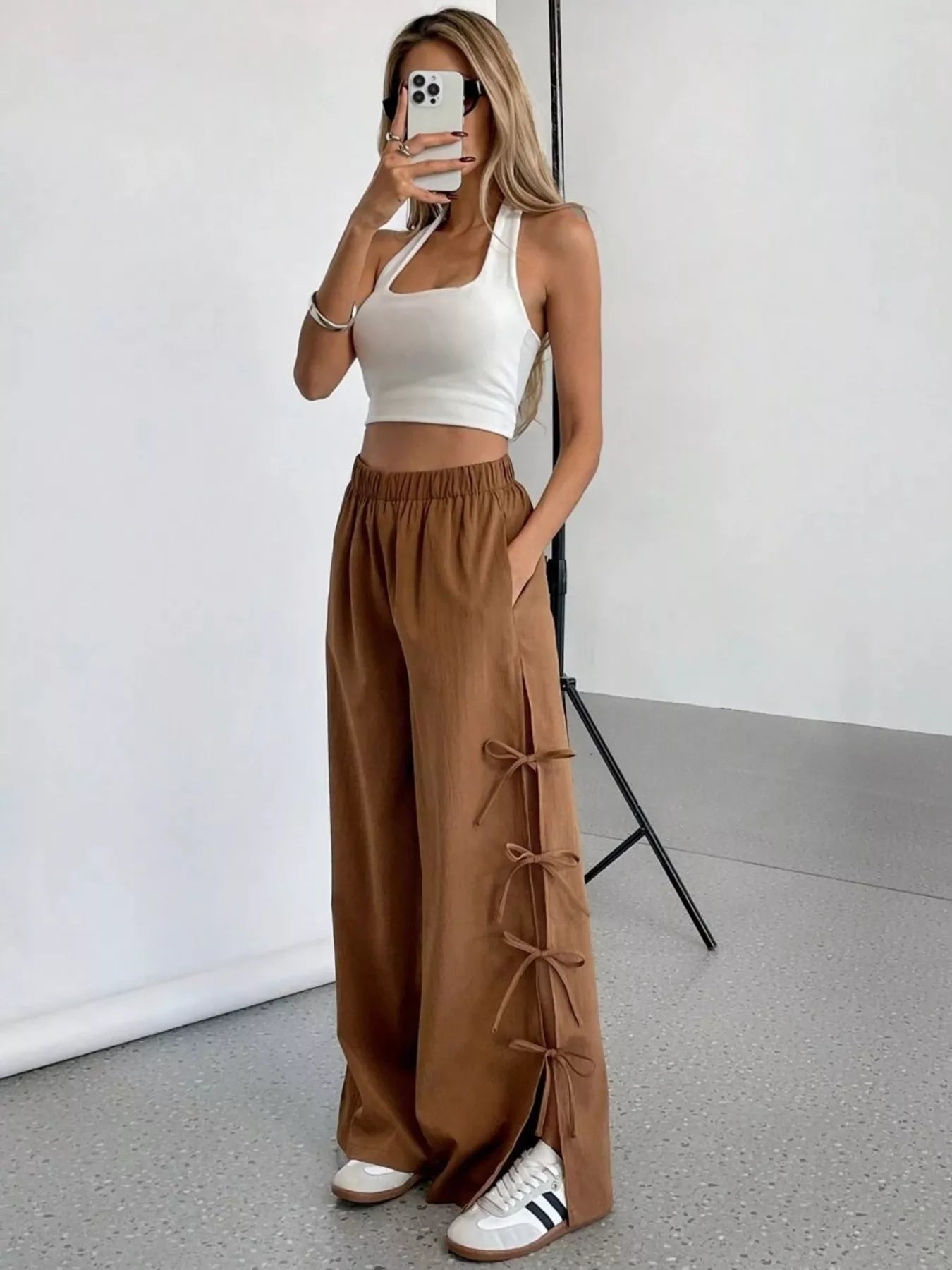 Person wearing a white top and brown wide-leg pants in a minimalistic setting.