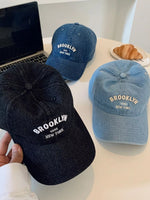 Three 'Brooklyn New York' caps on a table with a laptop and croissant in the background.