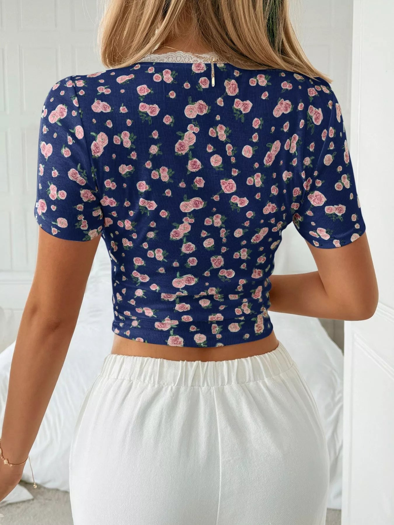 Person wearing a navy blue floral crop top with white pants indoors.