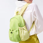 Person wearing a light green backpack with a white shirt and yellow pants on a plain background