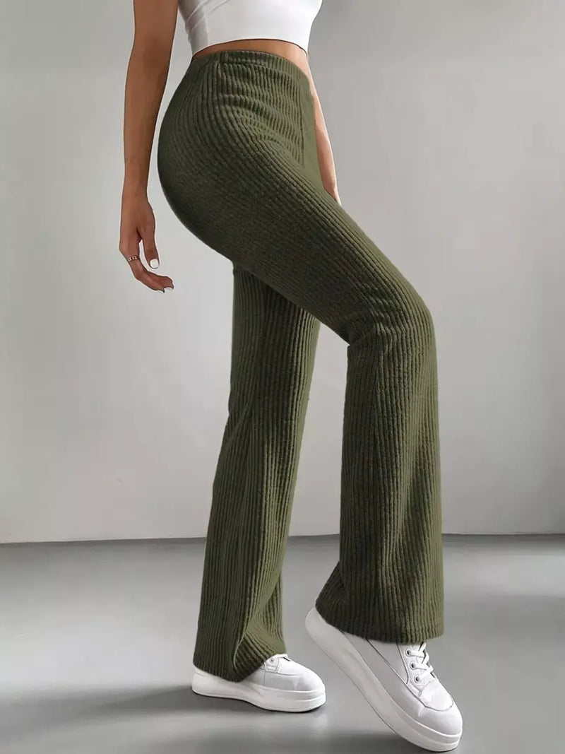 Person wearing green ribbed pants and white sneakers on a plain background