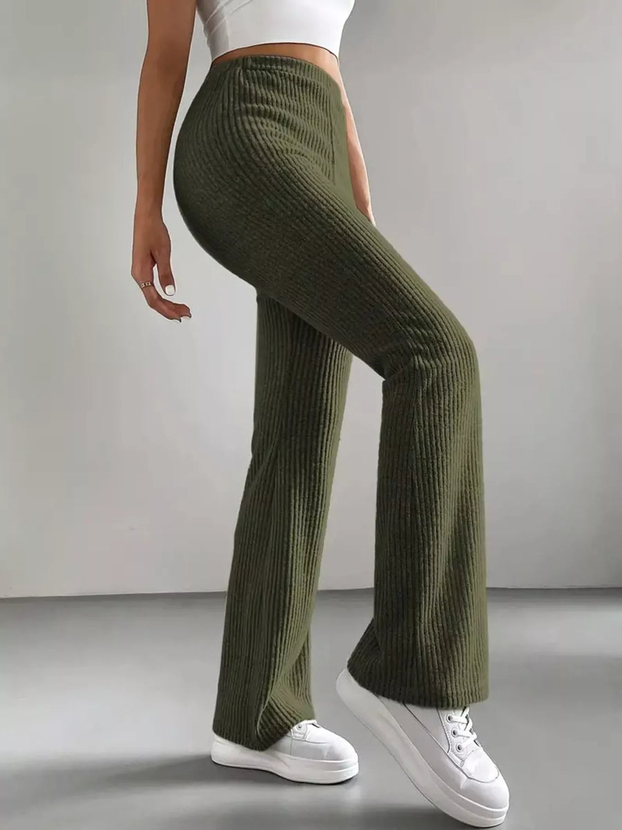 Person wearing green ribbed pants and white sneakers on a plain background
