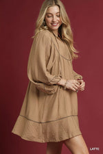 Woman wearing a beige dress with long sleeves against a red background