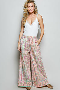 Woman wearing a white tank top and patterned wide-leg pants on a plain background
