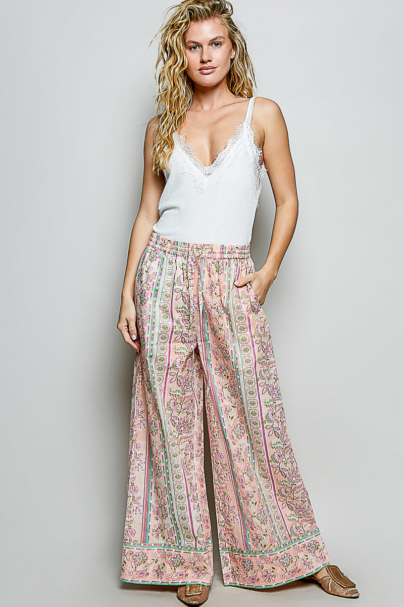 Woman wearing a white tank top and patterned wide-leg pants on a plain background