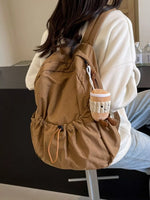 Person wearing a brown backpack with a plush toy attached, sitting indoors.