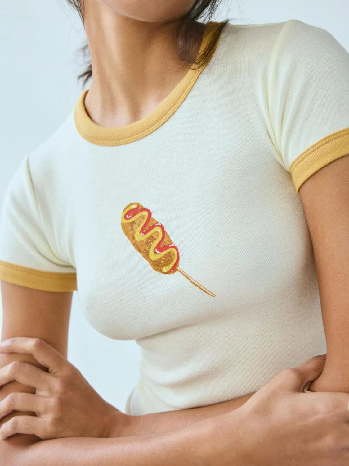 Person wearing a white t-shirt with a corn dog graphic on a light blue background