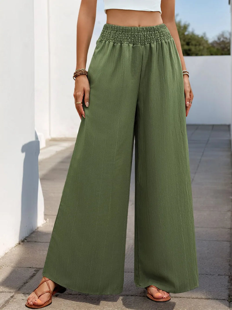 Person wearing green wide-leg pants with a white top and sandals on a sunny day.