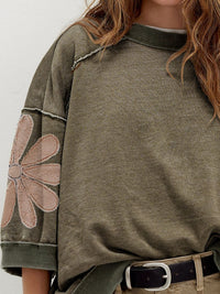 Green sweatshirt with floral designs on sleeves against a neutral background