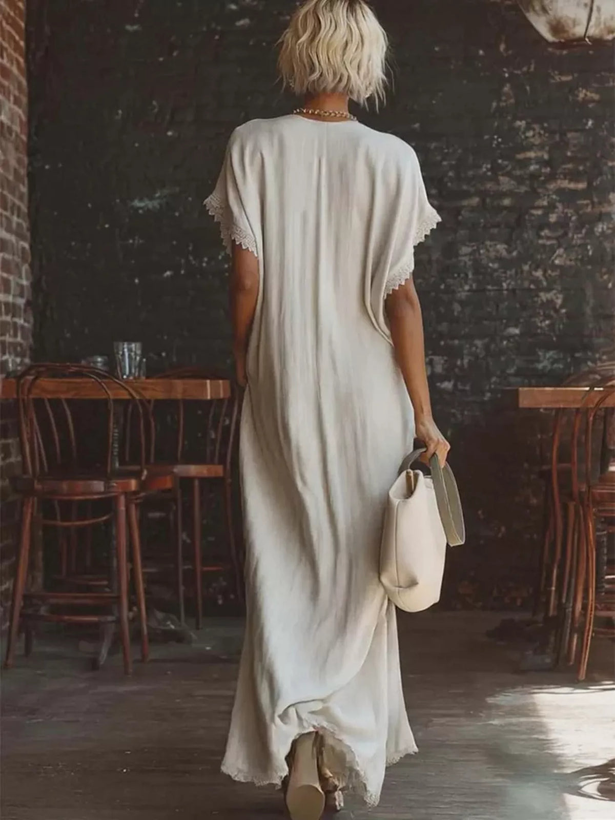 Woman in a long, light-colored dress walking through a rustic interior setting with wooden tables and chairs.